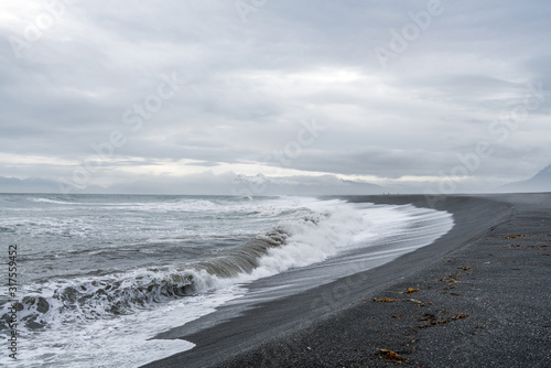 Waves crash ashore on Hvalnes beach with black lava sand on Hvalnes peninsula in southern Iceland. Traveling and photgraphy concept. Tourists in the background. photo