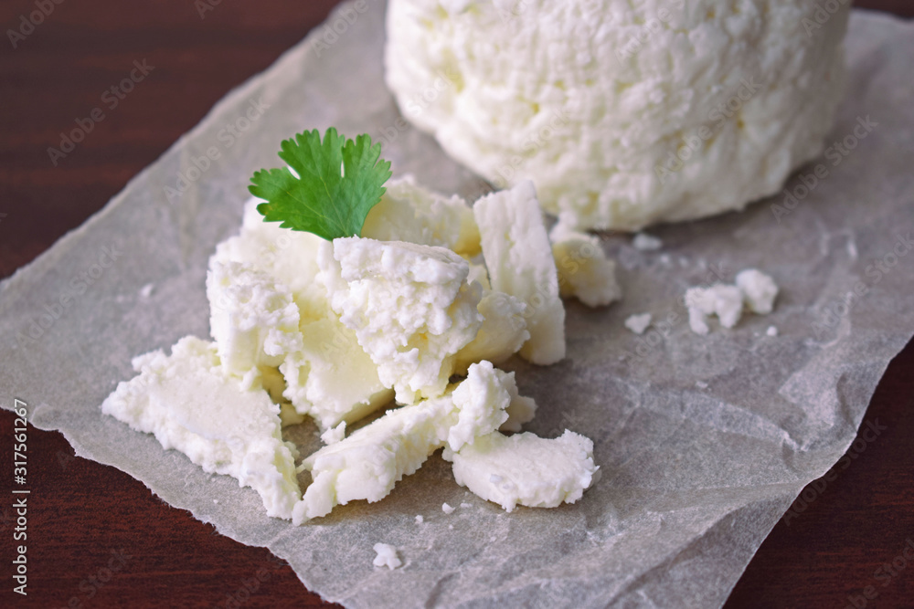 Homemade cheese with a sprig of greenery on a wooden background.