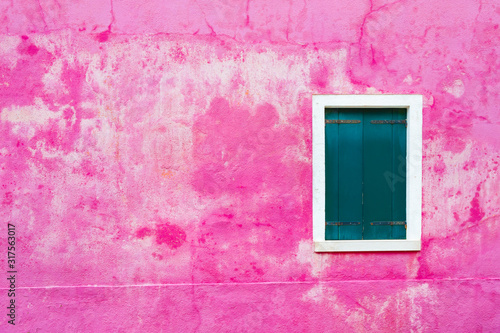 Window with green shutters on the shabby pink wall. Colorful architecture in Burano island, Venice, Italy.