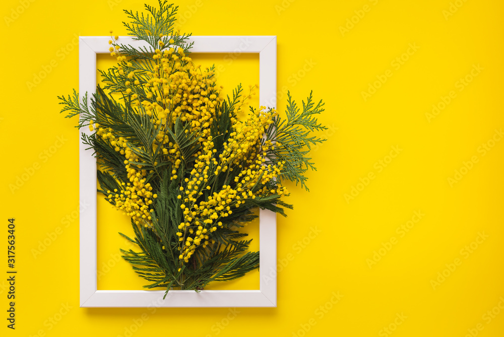 Fototapeta Mimosa flowers and green branches  on yellow pattern texture of crumpled paper with white photo frame, yellow background. Spring and Easter Frame Concept, flat lay, blank space