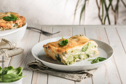 Italian lasagna with spinach and broccoli on white plate on bright background with copyspace.