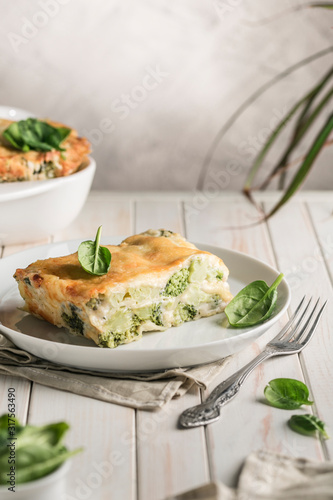 Italian lasagna with spinach and broccoli on white plate on bright background with copyspace.