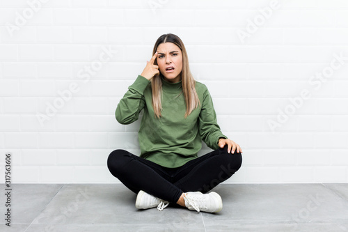Young caucasian woman sitting on the floor showing a disappointment gesture with forefinger.