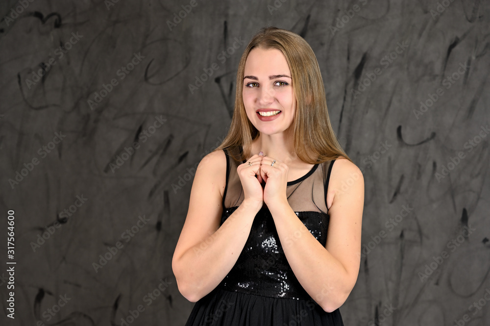 Naklejka premium Universal concept of horizontal female portrait on gray alternative background. A photo of a pretty smiling girl with long hair and excellent make-up in a black dress stands in different poses.