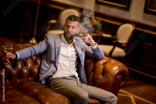 Young man tasting white wine and smoking cigar photo