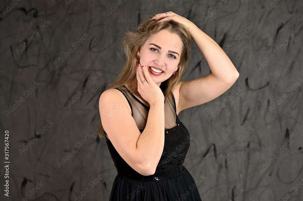 A photo of a pretty smiling girl with long hair and excellent make-up in a black dress stands in different poses. Universal concept of horizontal female portrait on gray alternative background. A photo of a pretty smiling girl with long hair and excellent make-up in a black dress stands in different poses. Universal concept of horizontal female portrait on gray alternative background.