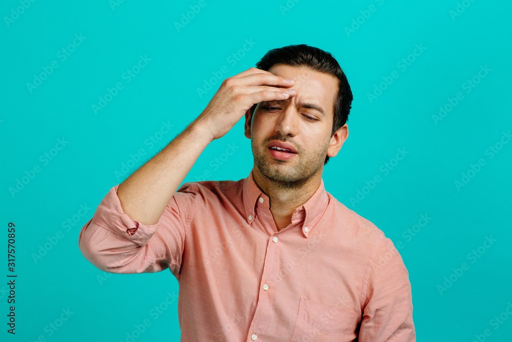 Portrait of a young adult man with a headache, isolated on blue studio background Portrait of a young adult man with a headache, isolated on blue studio background