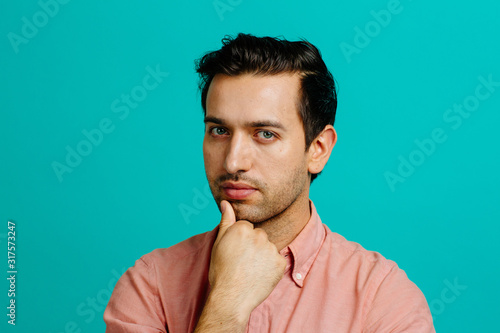 Portrait of a young adult man thinking, isolated on blue studio background