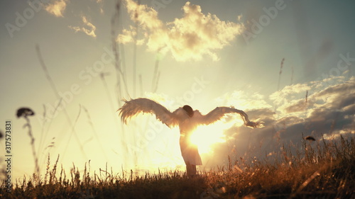 White angel and sun. Brunette girl in a white dress raises angel wings up, looks at the sun photo