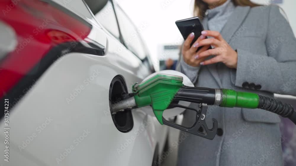 Woman using smartphone while her car is refueling. Slow motion Woman using smartphone while her car is refueling. Slow motion