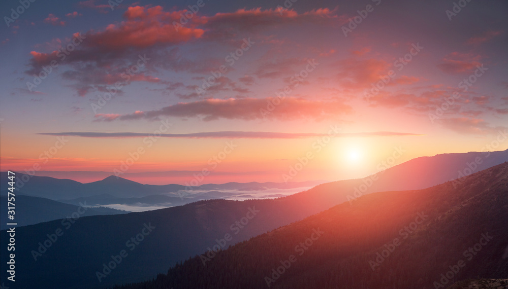 Panoramic landscape of colorful sunrise in the mountains. View on foggy hills covered by forest. Concept of the awakening wildlife.