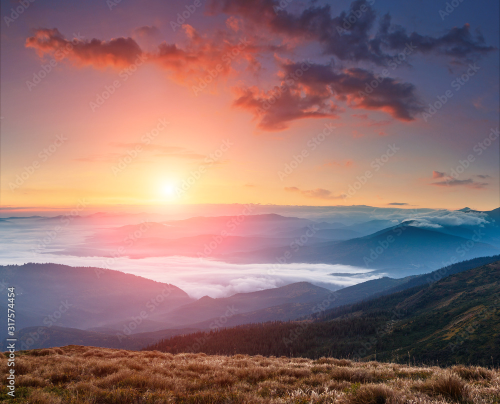 Landscape of colorful sunrise in the mountains. View on foggy hills covered by forest. Concept of the awakening wildlife.