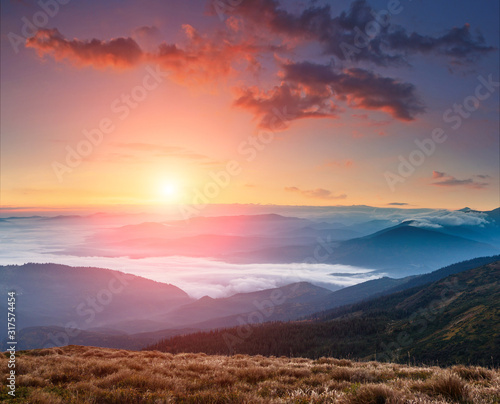 Landscape of colorful sunrise in the mountains. View on foggy hills covered by forest. Concept of the awakening wildlife.