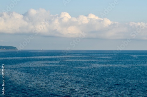 The black sea is blue with three bargeships with a cloud and a small piece of land passing along the horizon.