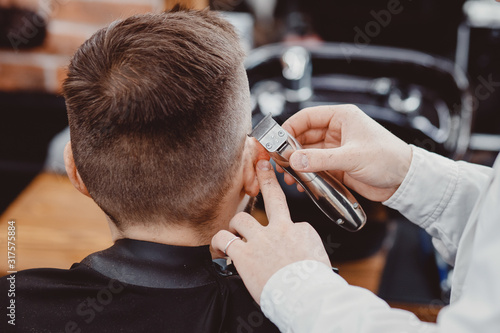 Hairdresser cuts hair young men in barbershop. Barber doing styling with electric shaver