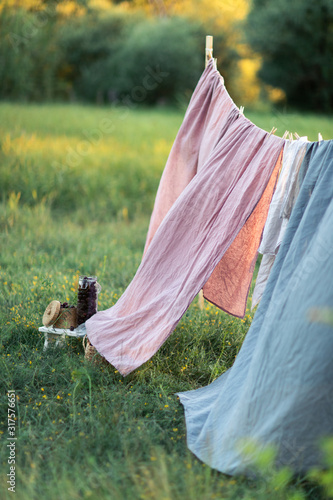 Pink and blue bedding sheet on forest background under the bright warm sun. Clean bed sheet hanging on clothesline at backyard. Hygiene sleeping ware concept.