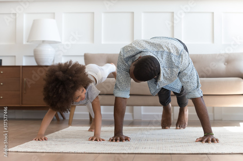 African father and little daughter do push-up exercise indoors photo