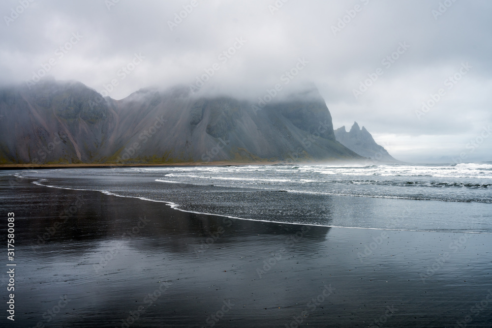 © Jon Anders Wiken - Waves are crashing ashore on Stokksnes peninsula black beach with vestrahorn mountain chain in the background. Travel and landscapes in Iceland concept.