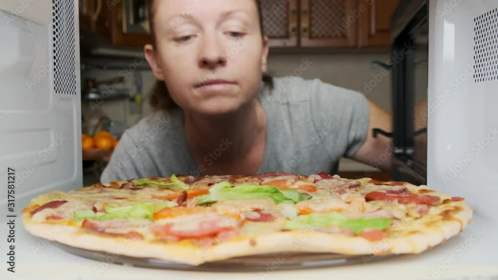 woman enjoys smell of cooked pizza in microwave oven. pizza with cheese and sausage cooking in microwave. woman enjoys smell of cooked pizza in microwave oven. pizza with cheese and sausage cooking in microwave.