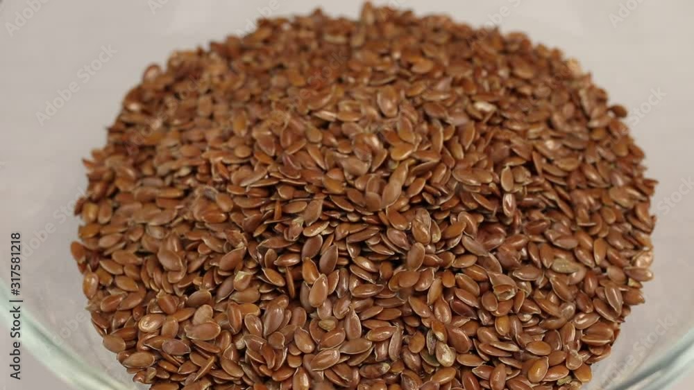 Flax seeds fall in a glass transparent bowl, close-up Flax seeds fall in a glass transparent bowl, close-up