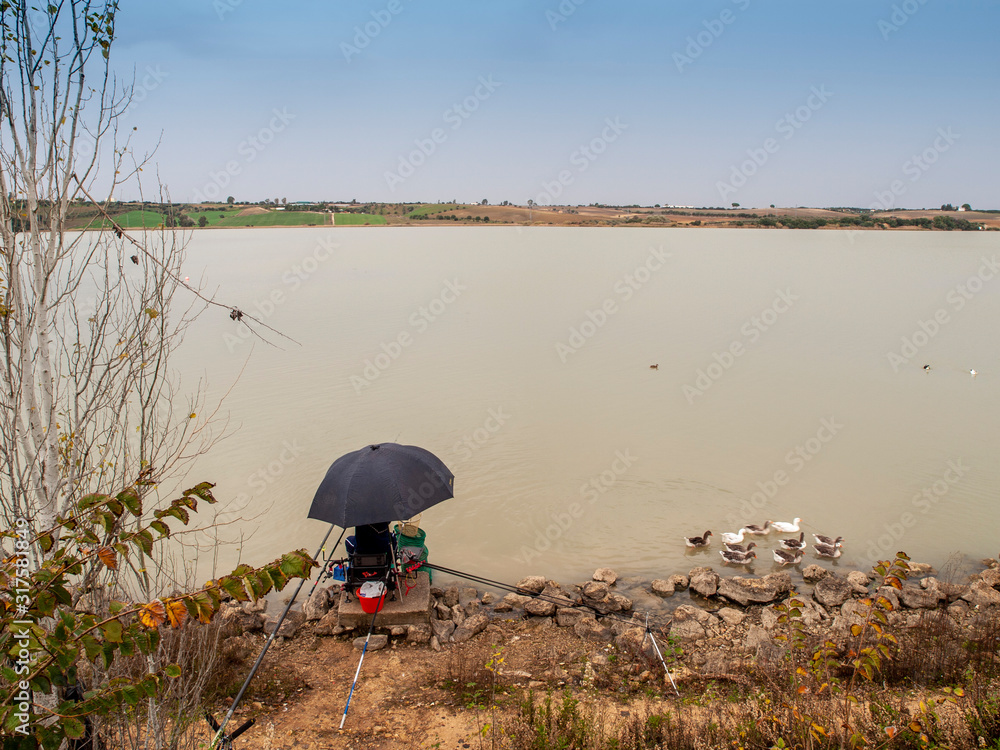 Pescador bajo sombrilla negra esperando a que piquen los peces en un lago de Cadiz