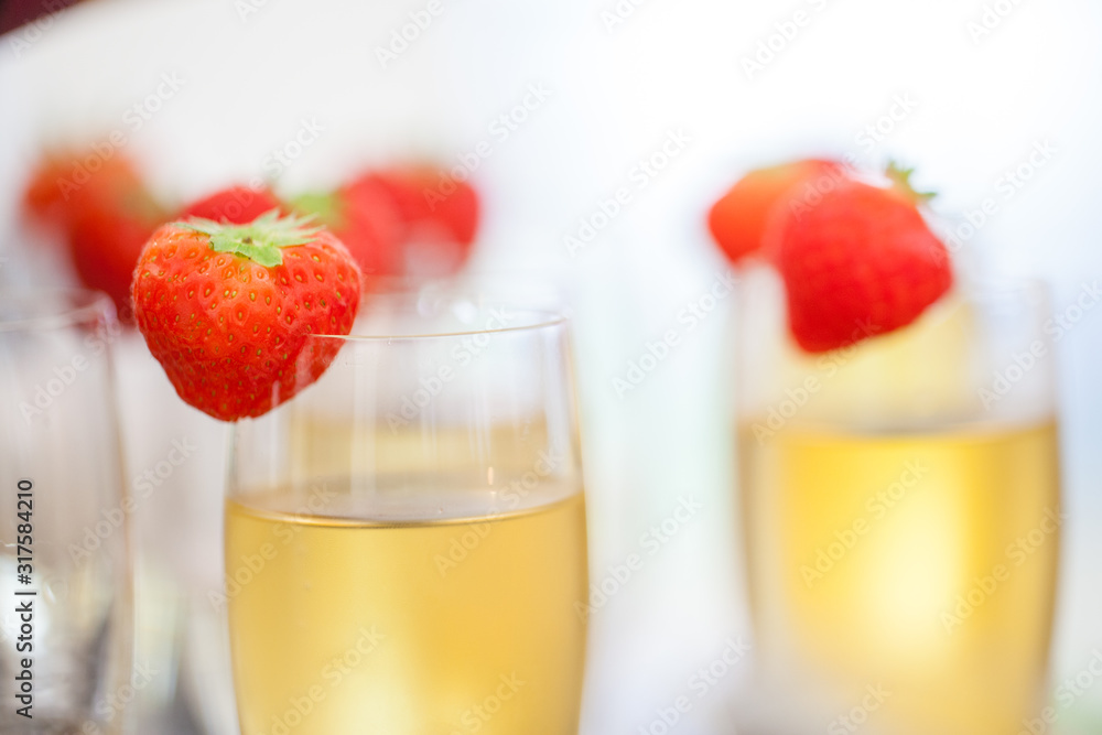 Close up of glasses of sparkling wine or champagne and strawberry on a blurry background during some sort of festivity or celebration such as a wedding, borthday or newyear Close up of glasses of sparkling wine or champagne and strawberry on a blurry background during some sort of festivity or celebration such as a wedding, borthday or newyear