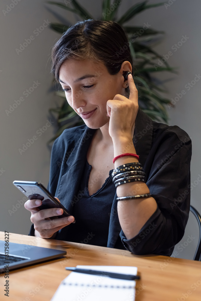 Shot of young woman working at home and using bluetooth headphones with the phone Shot of young woman working at home and using bluetooth headphones with the phone