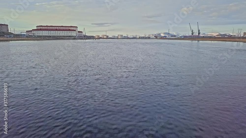 picturesque city buildings and constructions with cranes on river bank under cloudy sky aerial low angle motion above water