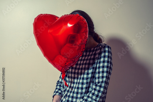 Girl hiding behind red heart shaped balloon. Valentines day and love concept.