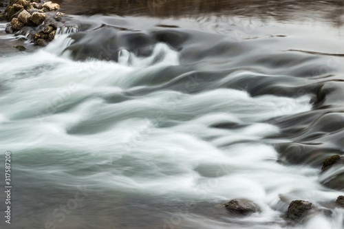 Abstract, long exposure shapes of the streaming river water passing over dark rocks