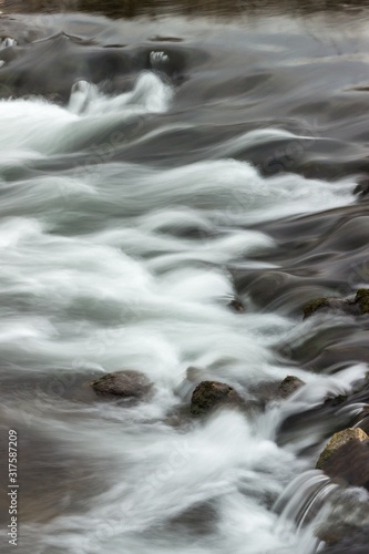 Abstract, long exposure shapes of the streaming river water passing over dark rocks