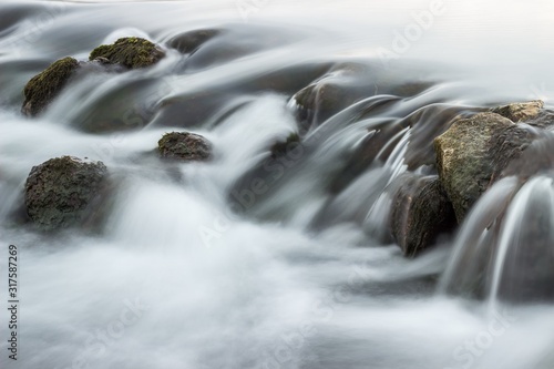 Abstract, long exposure shapes of the streaming river water passing over dark rocks photo