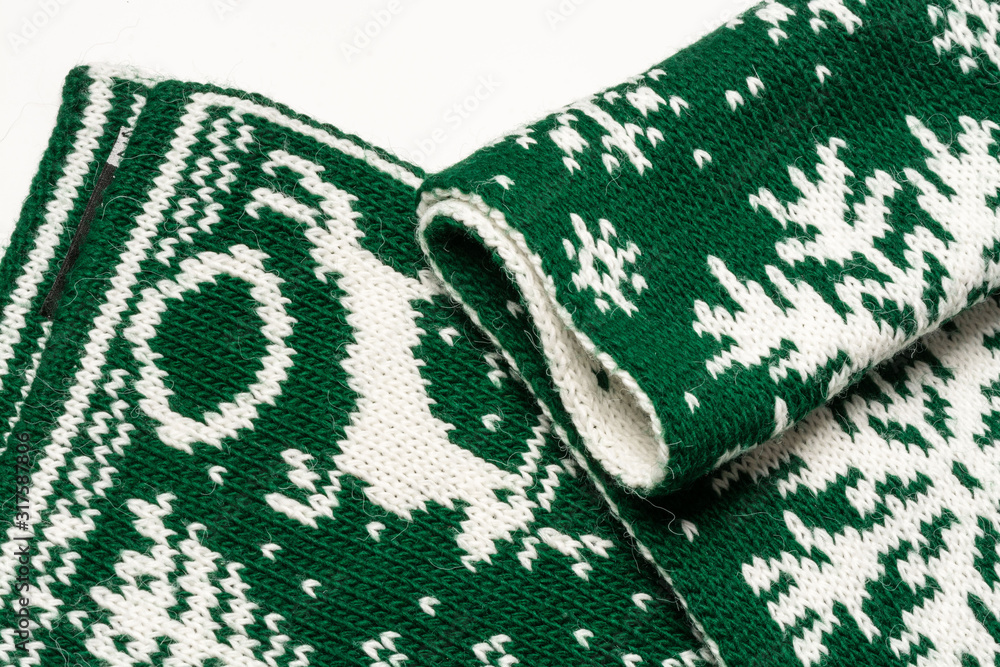 Fototapeta premium Fragment of a beautiful green scarf with white drawings depicting deer, spruce and snowflakes