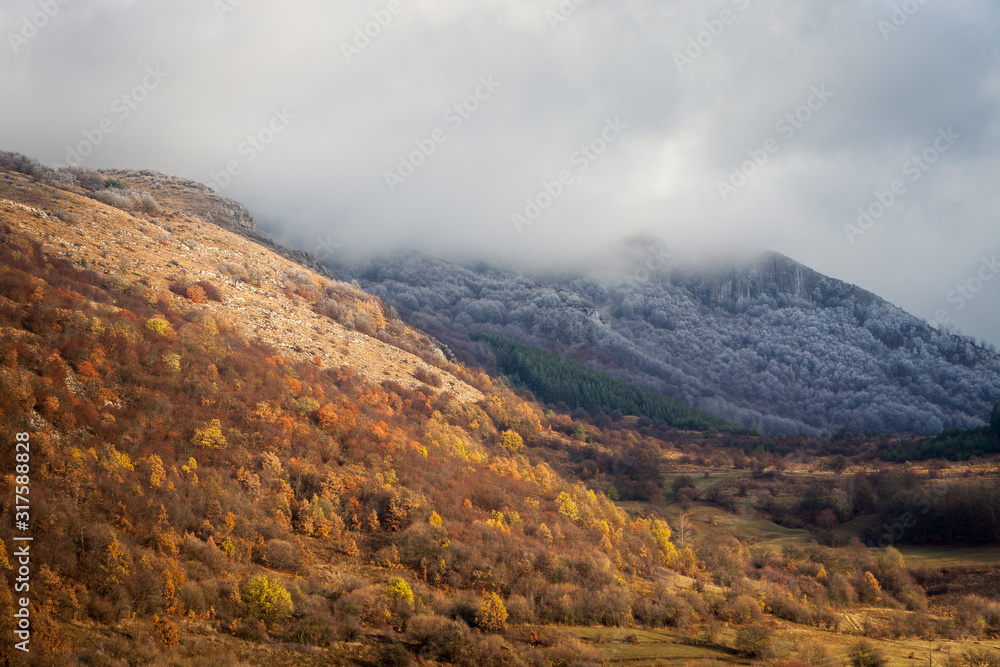 Amazing, moody, rocky summit covered in frost and fog, autumn colors of the forest trees below on the transition period between autumn and winter Amazing, moody, rocky summit covered in frost and fog, autumn colors of the forest trees below on the transition period between autumn and winter