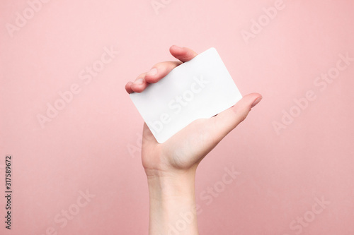 Female hand holding white business card on colorful pink background. Template, mockup, blank for web, social media, advertisement with copy space. Marketing, technology concept. Stock photo.