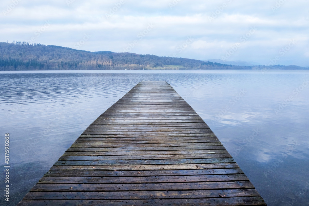 A long wooden jetty on a lake, jutting sraight out over a clear calm blue lake