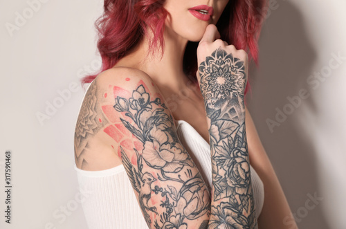 Beautiful woman with tattoos on body against light background, closeup photo