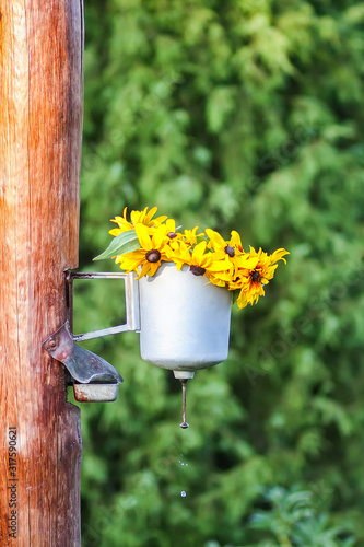 Old rural metal washstand with the wreath of yellow Rudbeckia flowers hanging on wooden pole on country yard
