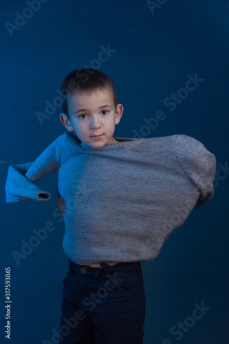Photos Studio portrait of a dark-haired boy wearing a gray sweater on a blue background