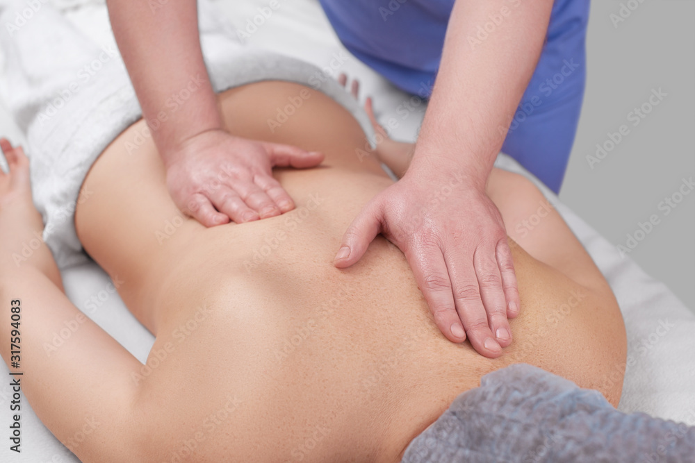 Masseur makes a relaxing massage on the neck, shoulders and  back of a young beautiful woman in a spa. Cosmetology and massage concept.