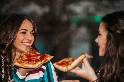 Portrait of two young women eating pizza outdoors  having fun together