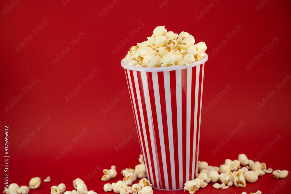 Butter popcorn in a red popcorn cup, snack in the house or cinema on a red background