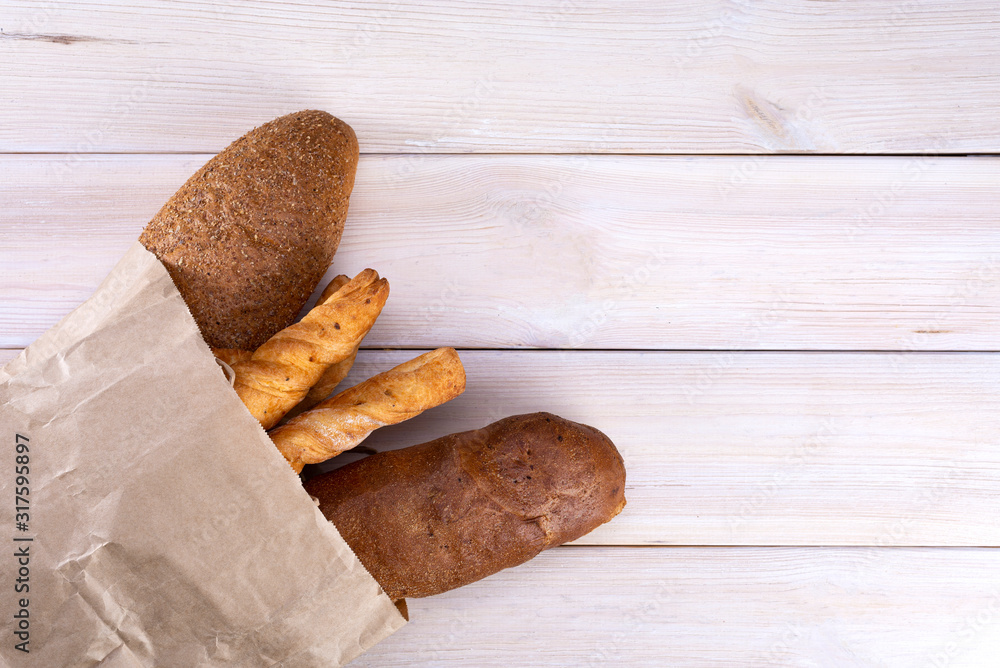 Bread in a paper bag on a light wooden background, top view