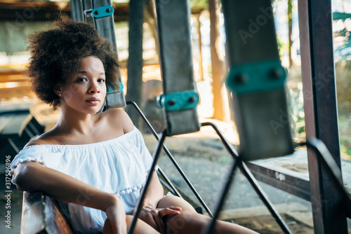 Portrait of beautiful happy young woman with afro sitting on bench swing 