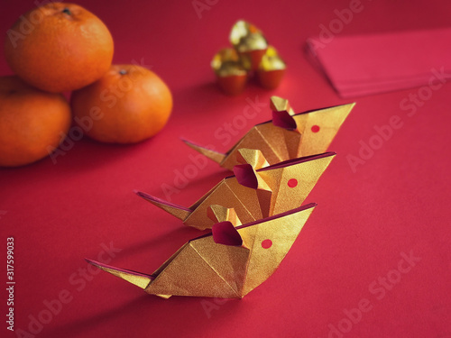 Chinese New Year concept. Golden origami rats, golden ingots, mandarin oranges and ang paos on red background.