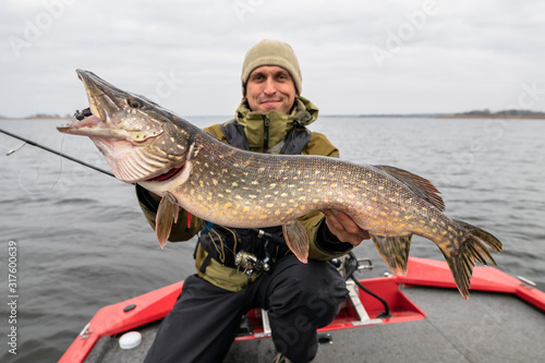 Pike fishing. Happy fisherman holding big fish at boat