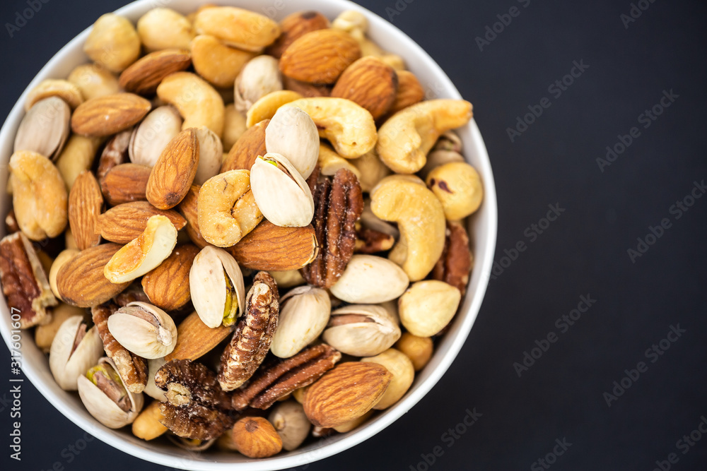Hazelnut ,Pecan nut, Pistachio nut ,Peanuts nut,Almond nut mixed salt in a wooden plate is Protein food and healthy food for diet food on a black background. Hazelnut ,Pecan nut, Pistachio nut ,Peanuts nut,Almond nut mixed salt in a wooden plate is Protein food and healthy food for diet food on a black background.