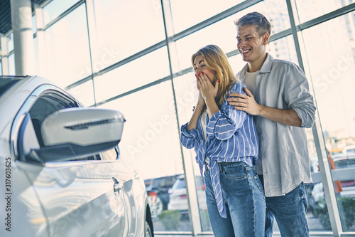 Happy girl before getting a present new car in showroom.