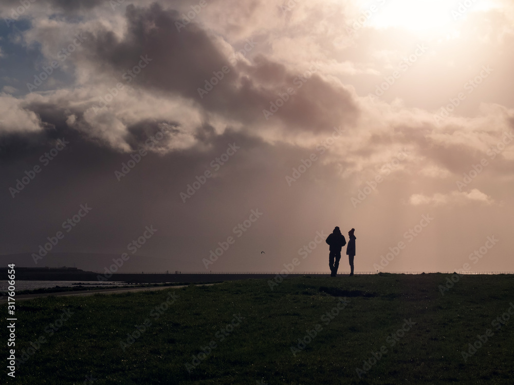 Silhouette of a couple walking and holding hand against beautiful cloudy warm sky, Sun flare. Concept romantic and love through body language.