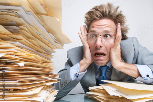 Stressed office worker looking with   shock at a massive stack of file folders on his desk photo